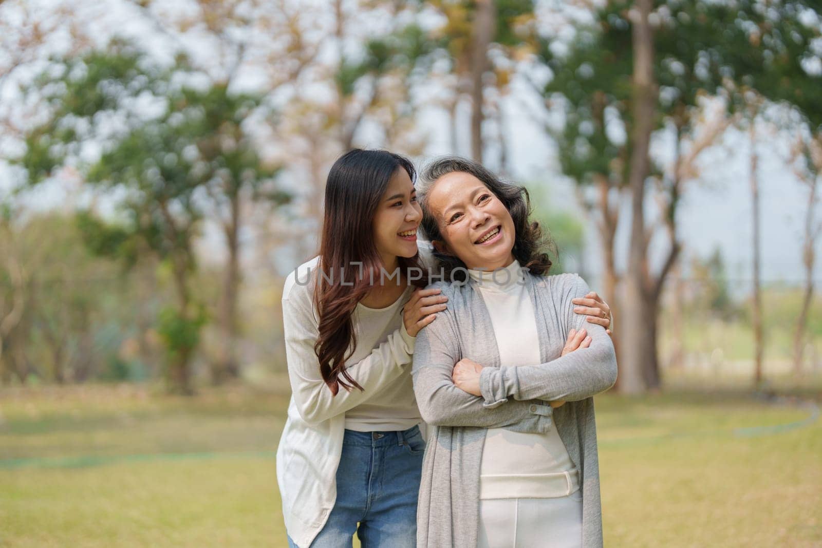 Grown daughter with aging mother showing love and walking together in the parkland by Manastrong