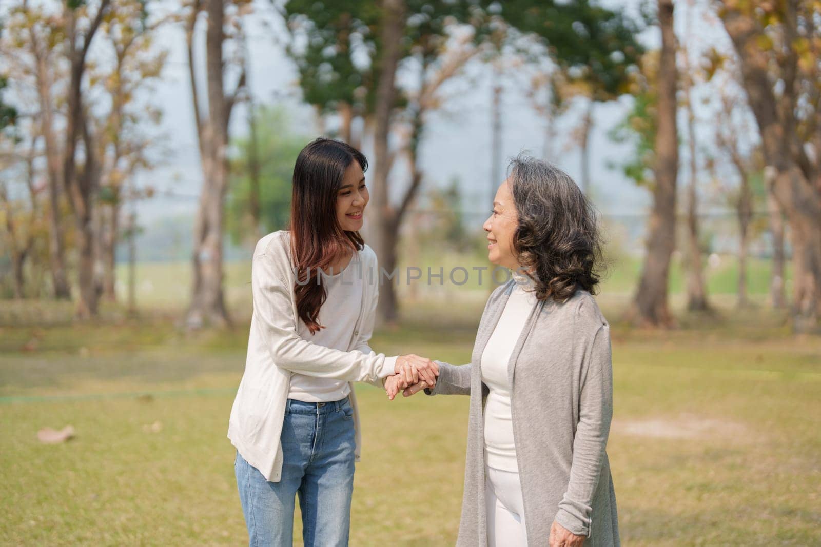 Adult daughter holding her elderly mother hand with love and walk together in park.