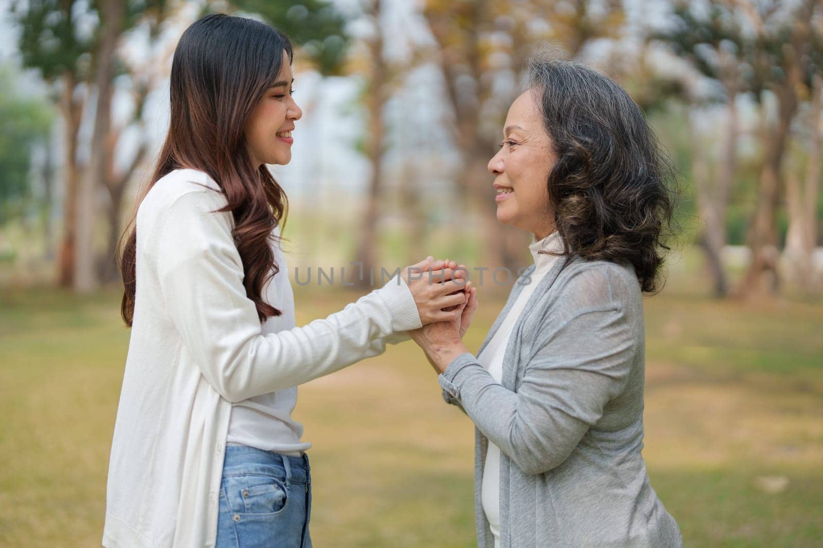 Adult daughter holding her elderly mother hand with love and walk together in park by Manastrong