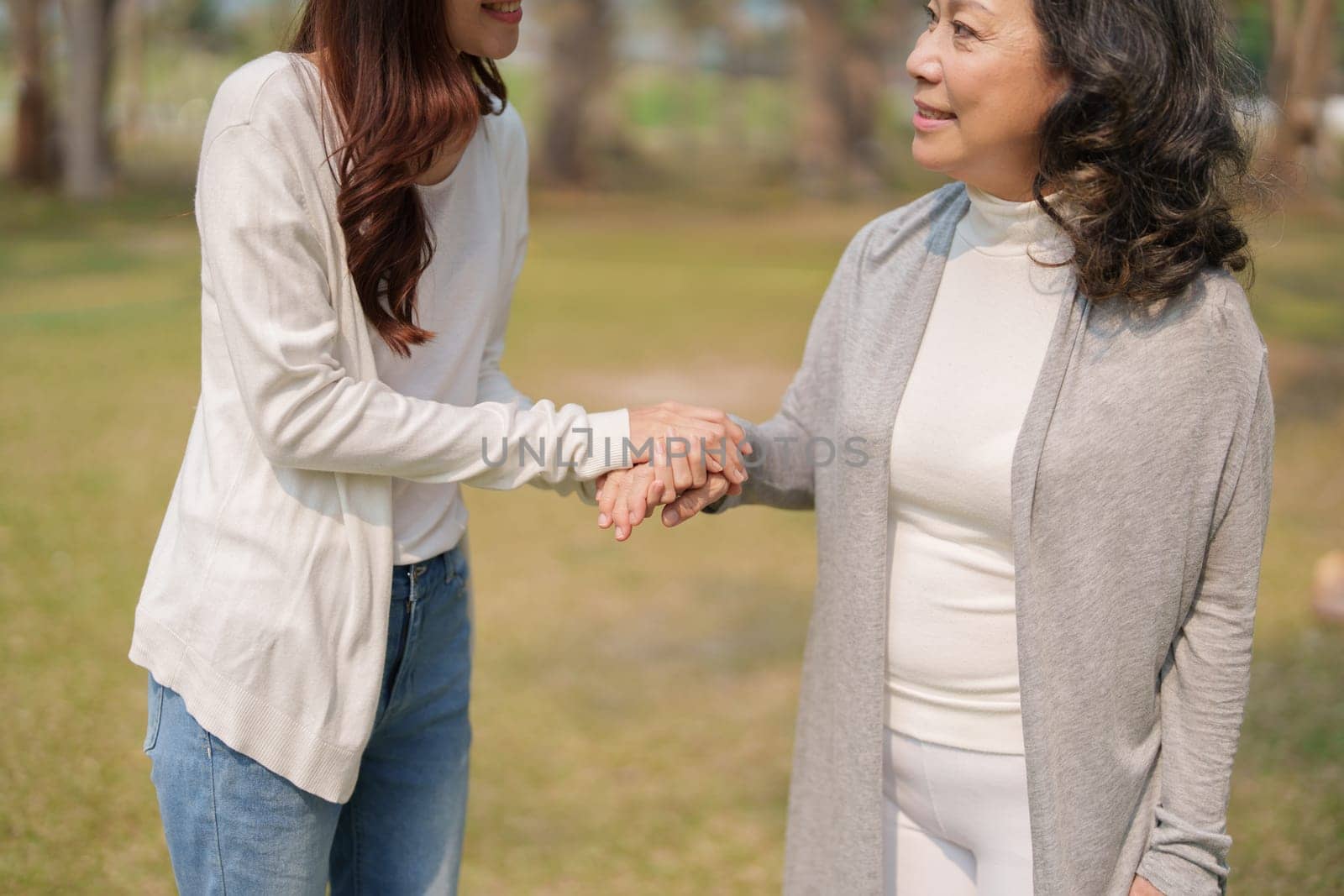 Adult daughter holding her elderly mother hand with love and walk together in park by Manastrong