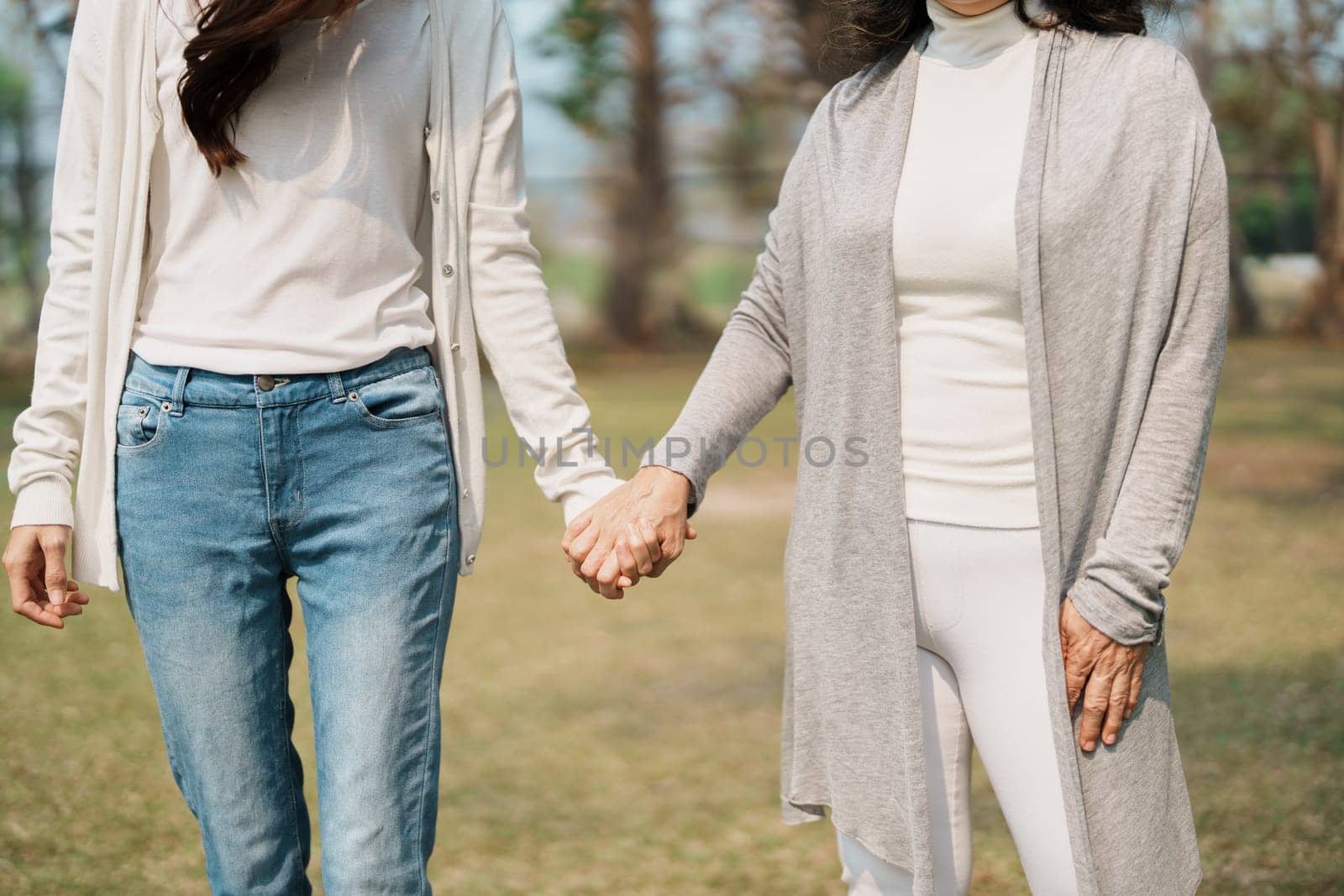 Adult daughter holding her elderly mother hand with love and walk together in park by Manastrong