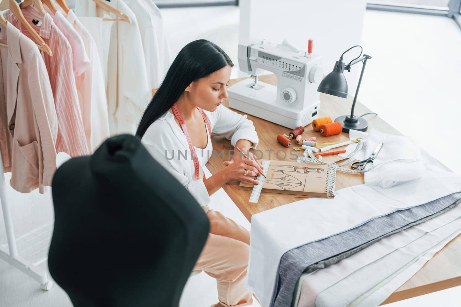 Sitting by the table. Seamstress is in her office that is with different clothes.