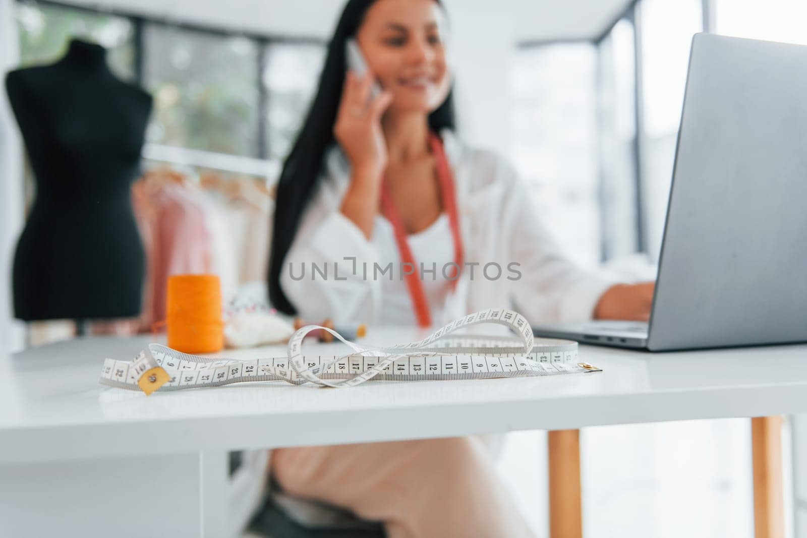 Using laptop. Seamstress is in her office that is with different clothes.