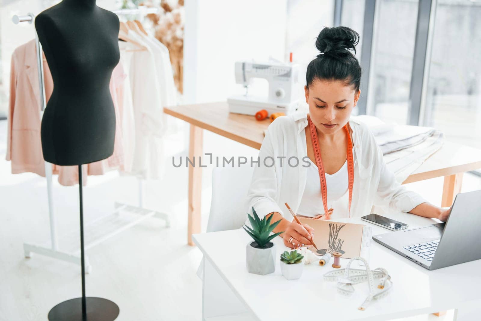 Using laptop. Seamstress is in her office that is with different clothes.