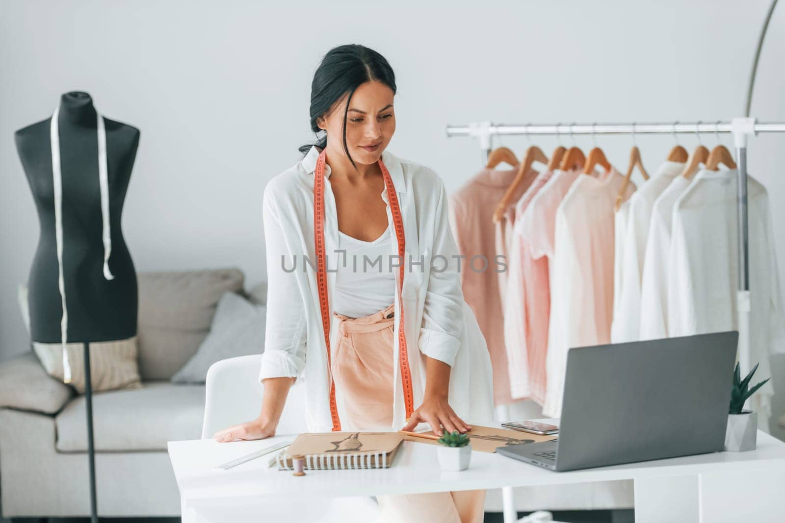 With laptop. Seamstress is in her office that is with different clothes.
