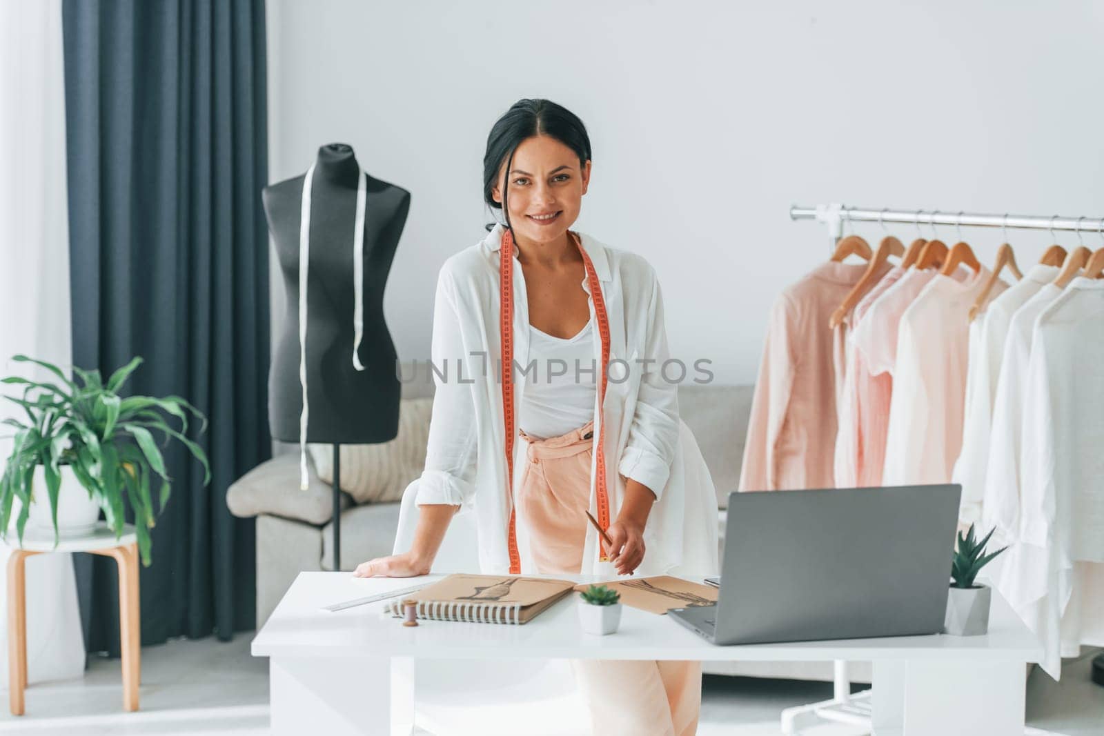 Seamstress is standing in her office that is with different clothes.