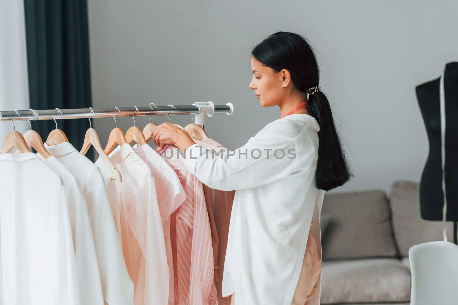 Seamstress is standing in her office that is with different clothes.