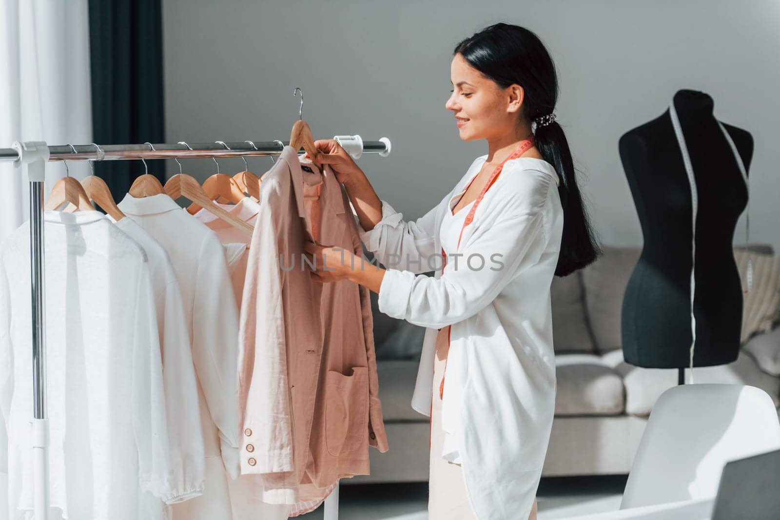 Seamstress is standing in her office that is with different clothes.