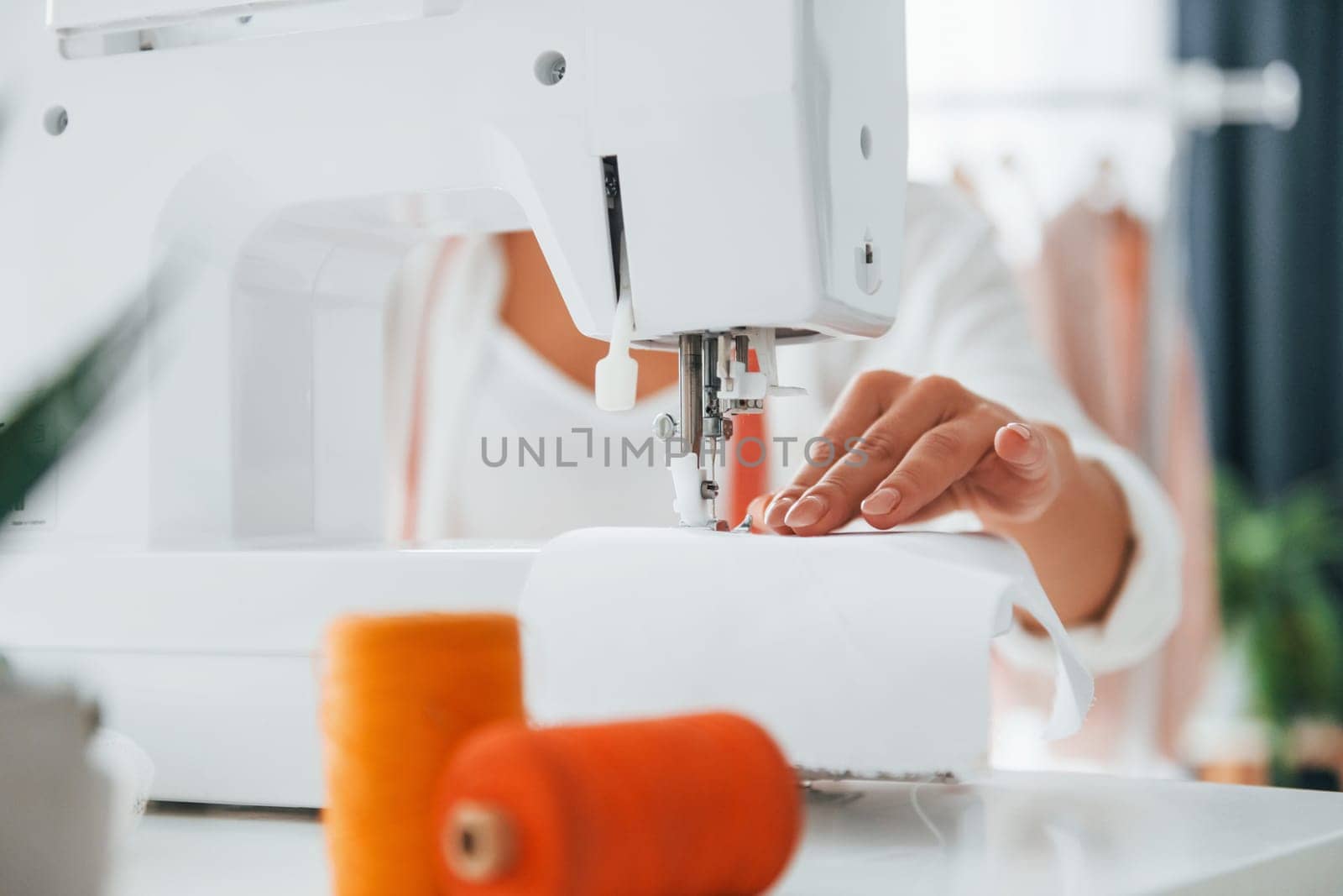 Working by using sewing machine. Seamstress is in her office that is with different clothes.