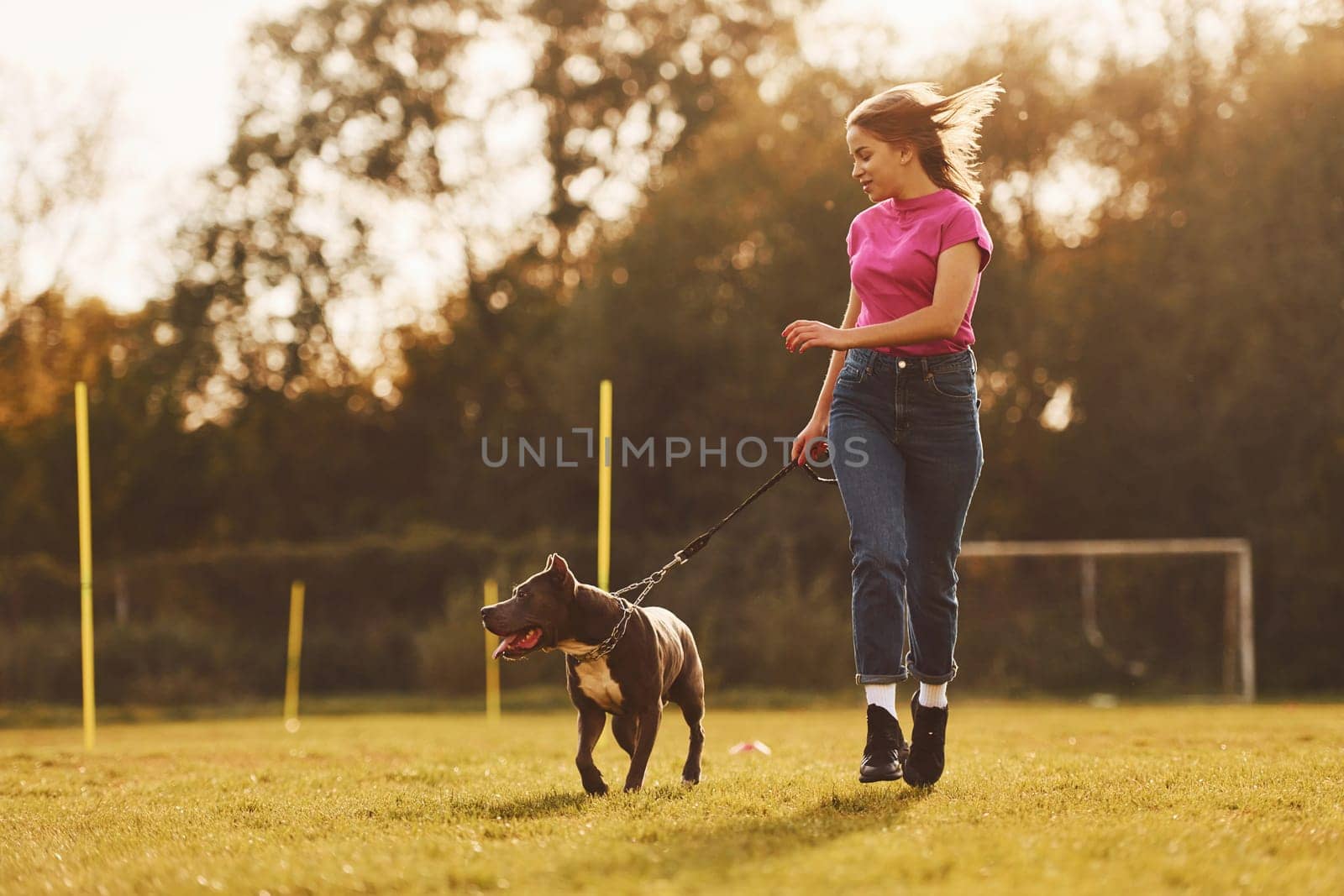 On sportive field. Woman in casual clothes is with pit bull outdoors.