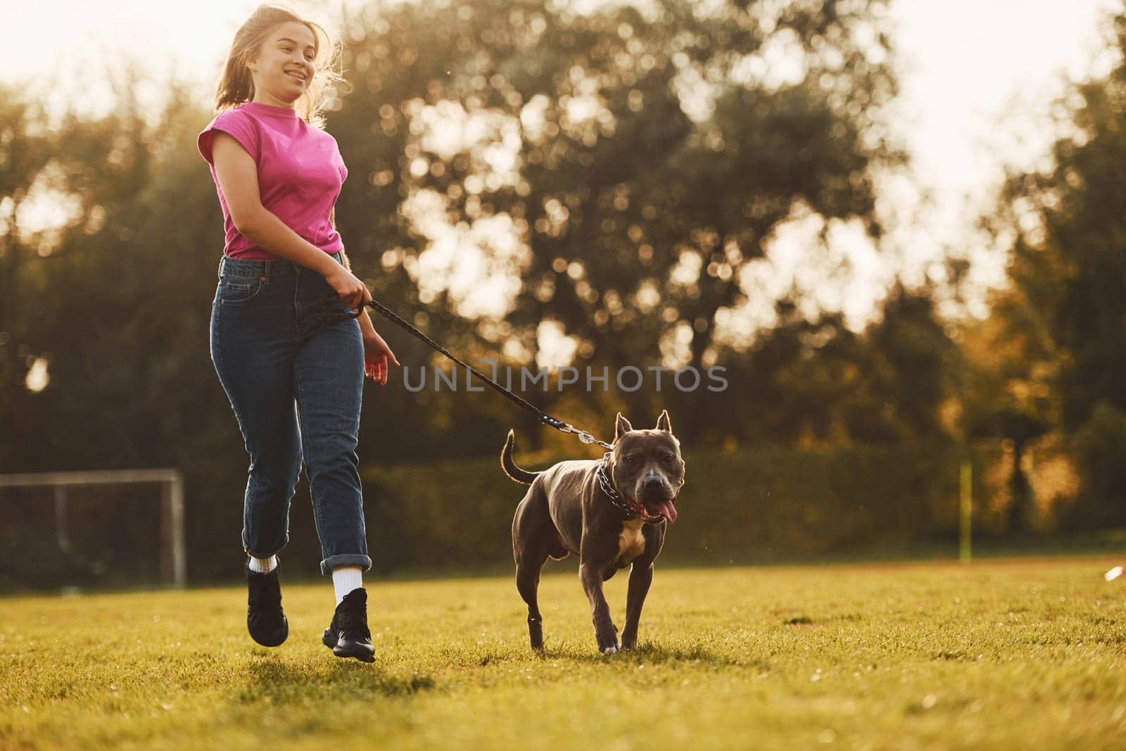 On sportive field. Woman in casual clothes is with pit bull outdoors.
