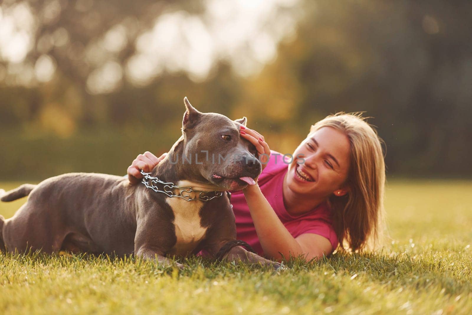 On the green grass. Woman in casual clothes is with pit bull outdoors.