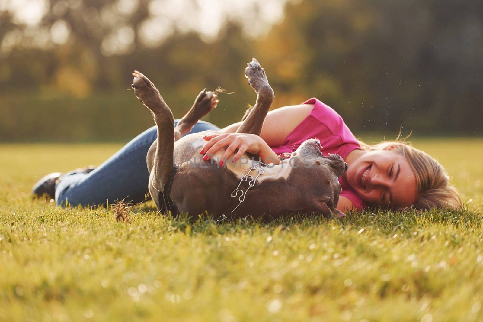 On the green grass. Woman in casual clothes is with pit bull outdoors.