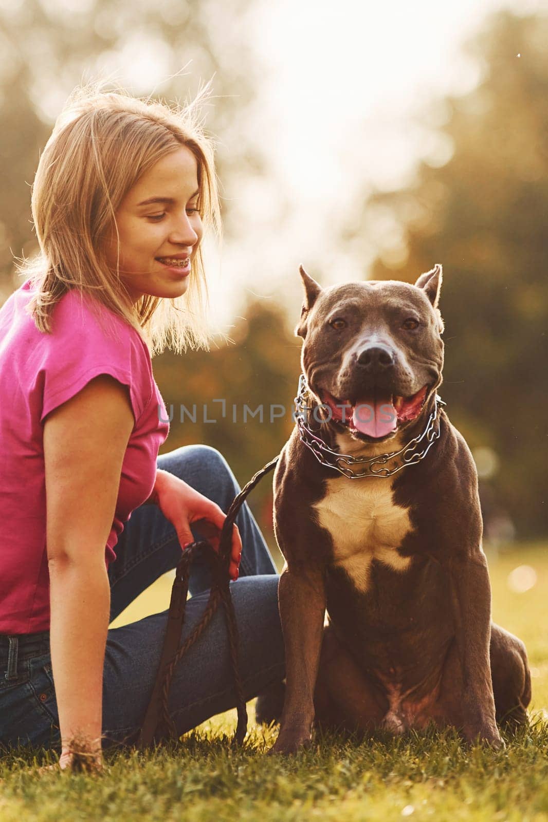 On the green grass. Woman in casual clothes is with pit bull outdoors.