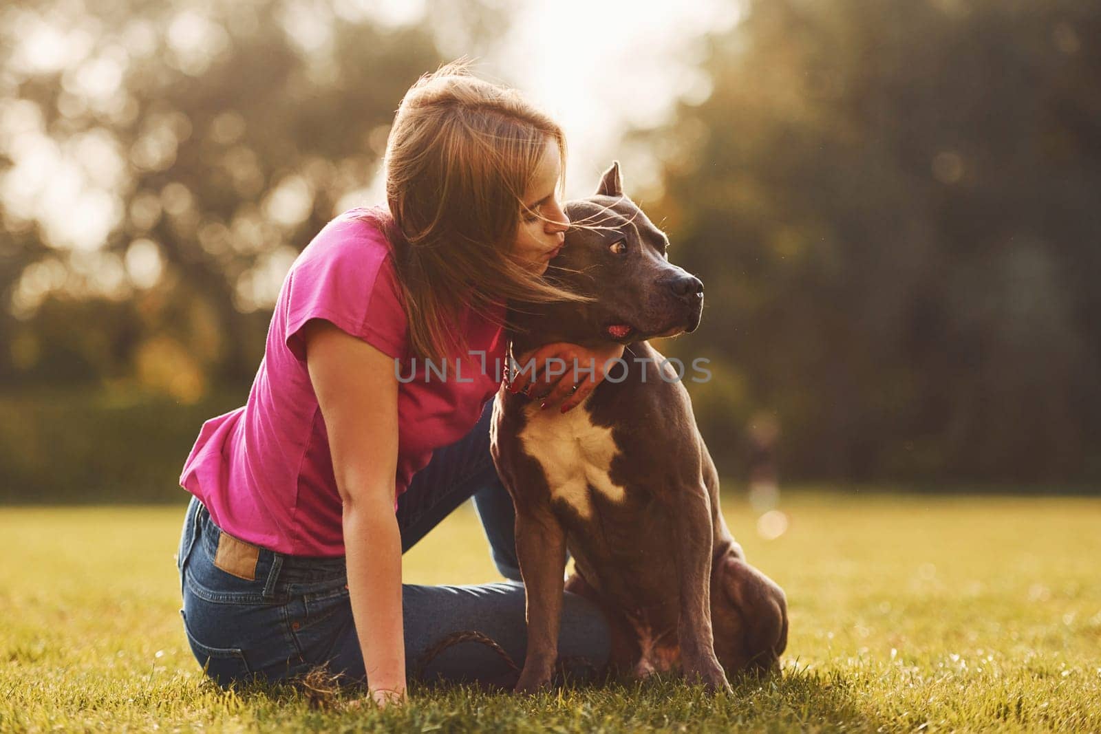 On the green grass. Woman in casual clothes is with pit bull outdoors.