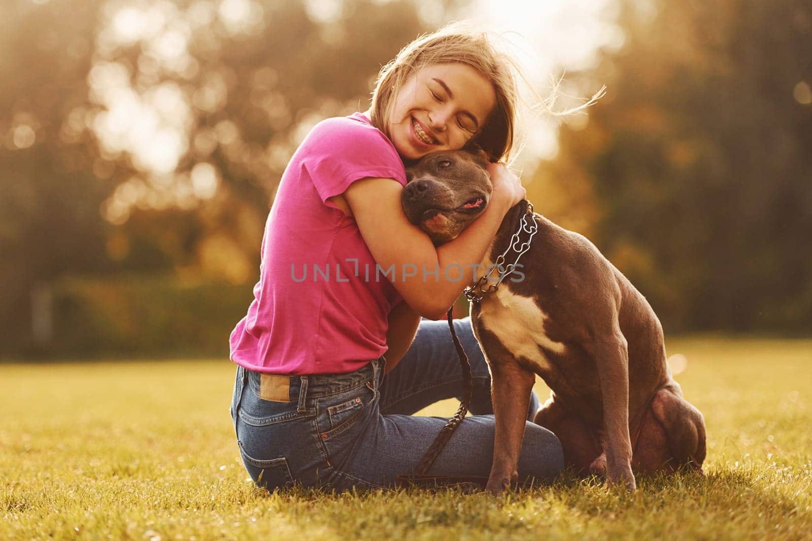 Embracing the dog. Woman in casual clothes is with pit bull outdoors.