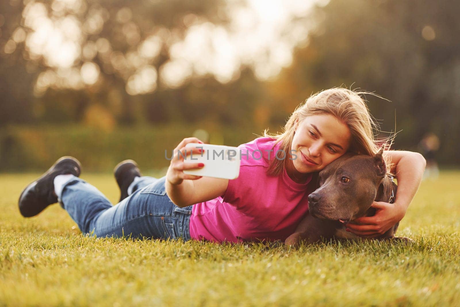 Making selfie. Woman in casual clothes is with pit bull outdoors.