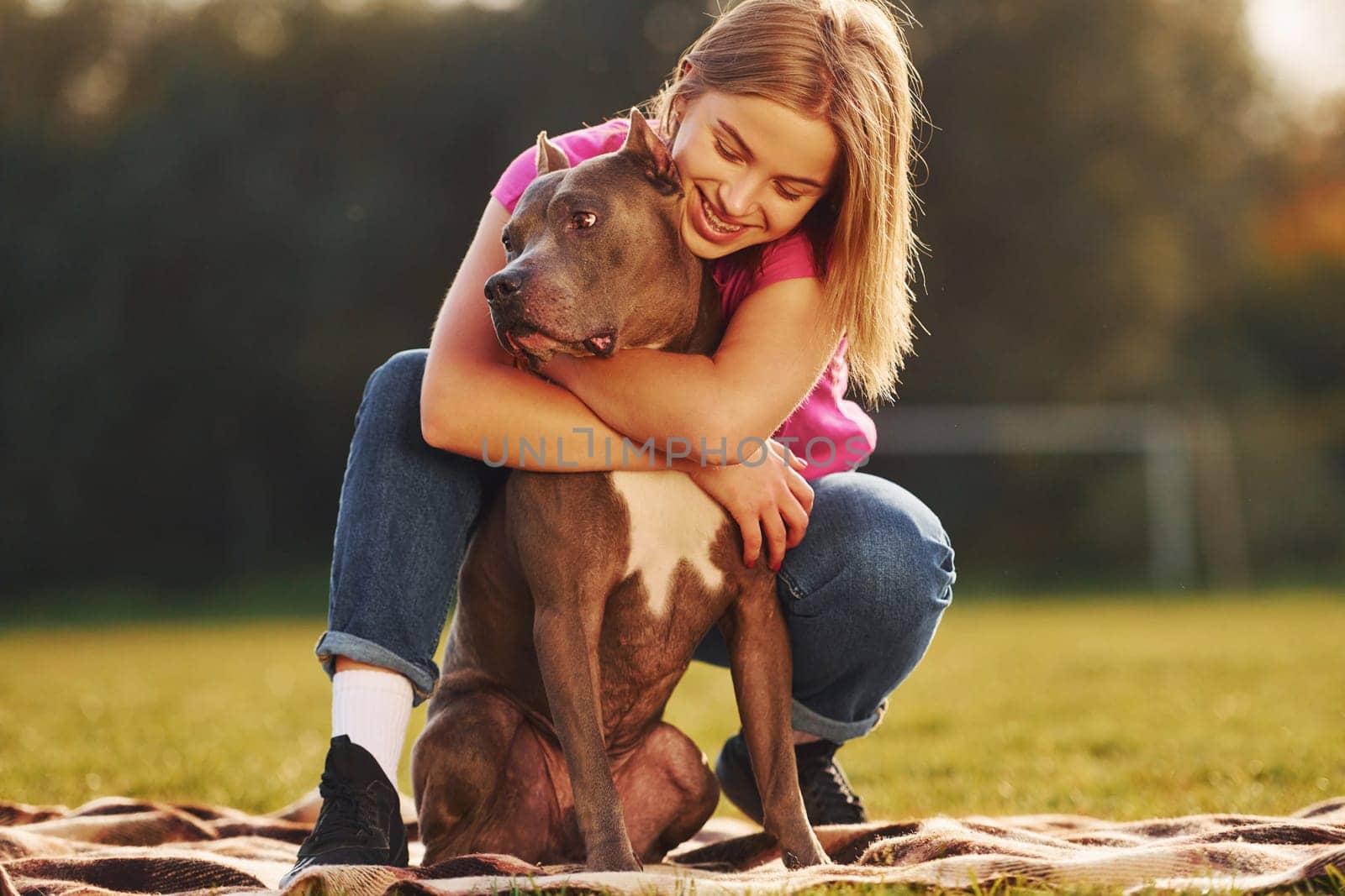 Lying down on a blanket. Woman in casual clothes is with pit bull outdoors.