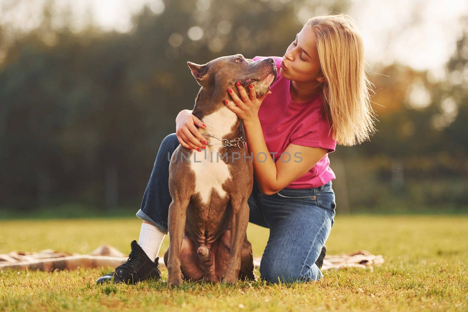 Positive emotions. Woman in casual clothes is with pit bull outdoors.