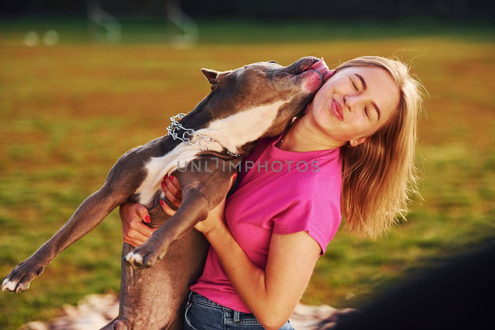 Positive emotions. Woman in casual clothes is with pit bull outdoors.