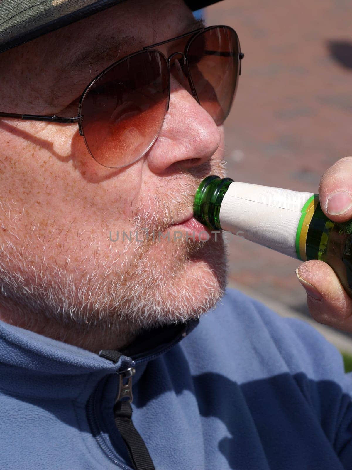 man in sunglasses drinking beer from bottle close-up by Annado