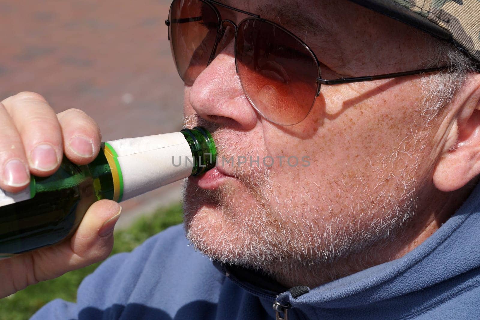 man in sunglasses drinking beer from bottle close-up by Annado