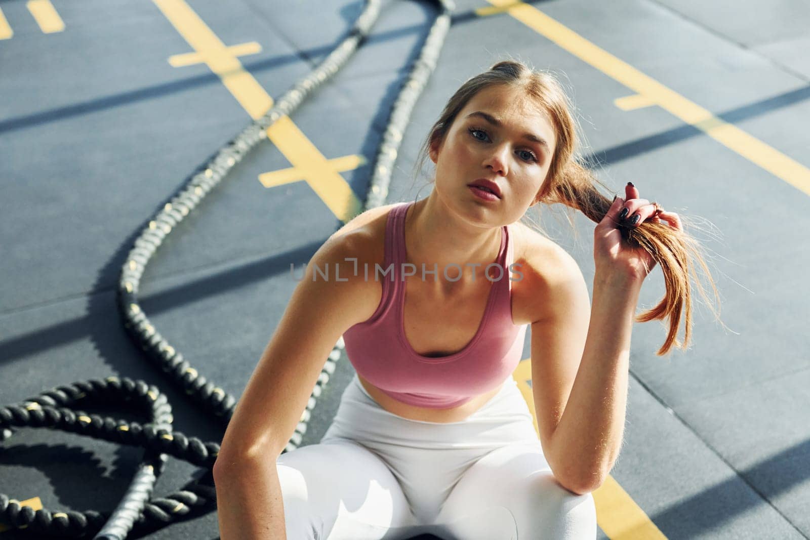 Sitting on the ground. Beautiful young woman with slim body type is in the gym.