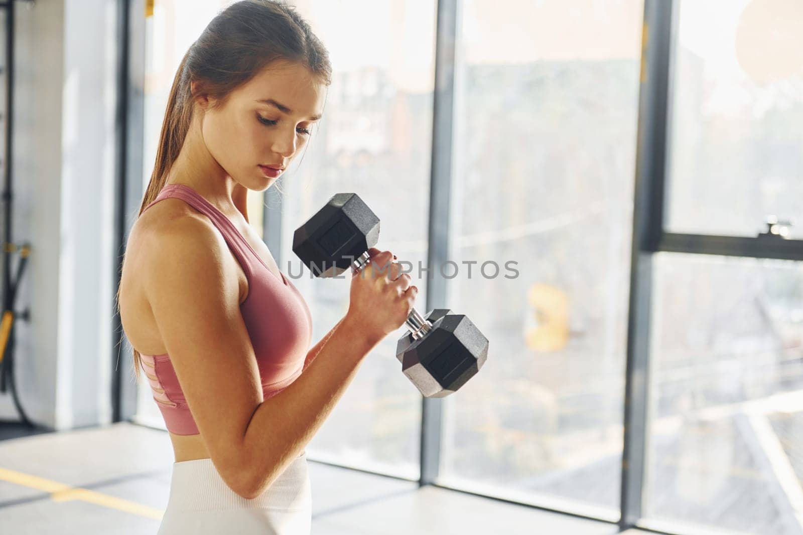 Standing with equipment. Beautiful young woman with slim body type is in the gym.