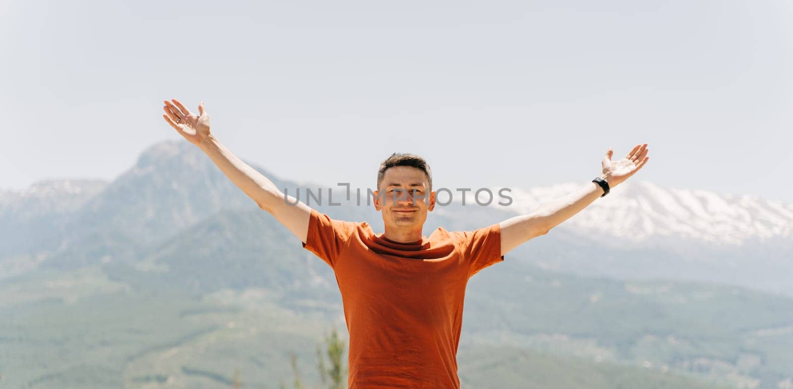 Portrait of Young man standing on Mountain View. Raised hands on mountain background by Ostanina