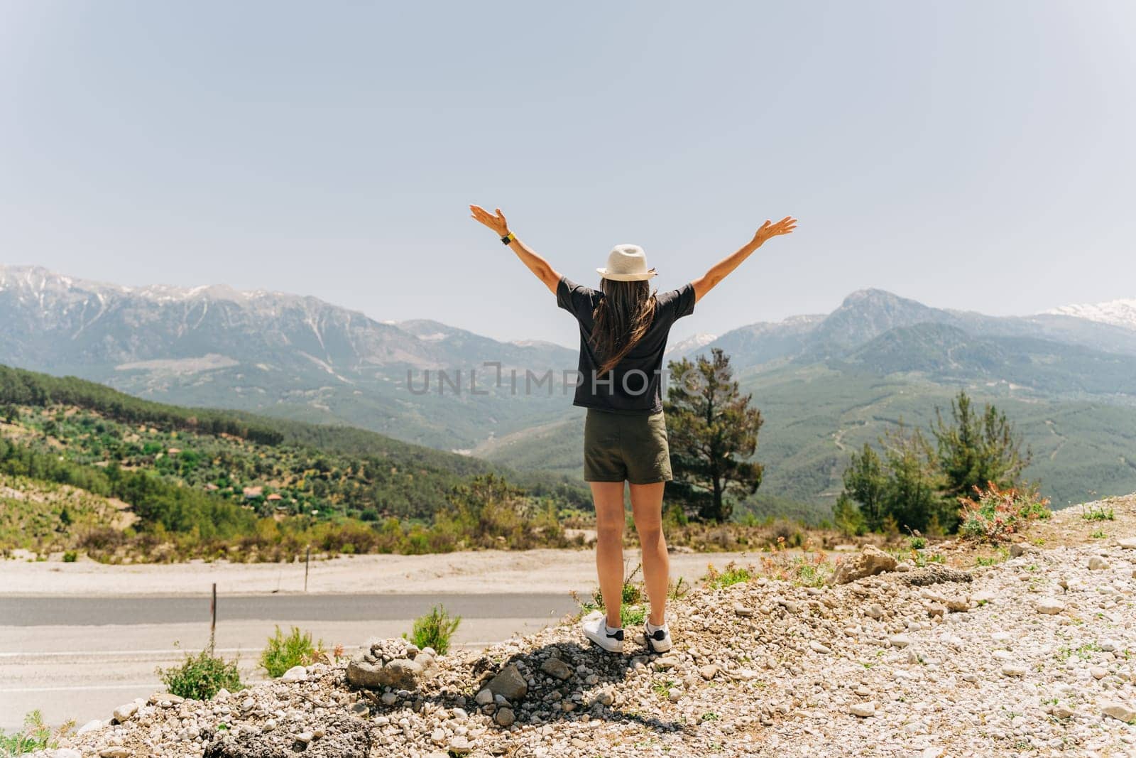 Young woman in hat standing on Mountain View. Raised hands on mountain background by Ostanina