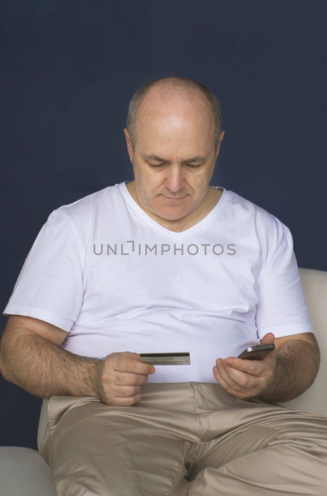 A man sits on a sofa, holds a smartphone and a credit card, makes payments via the Internet.