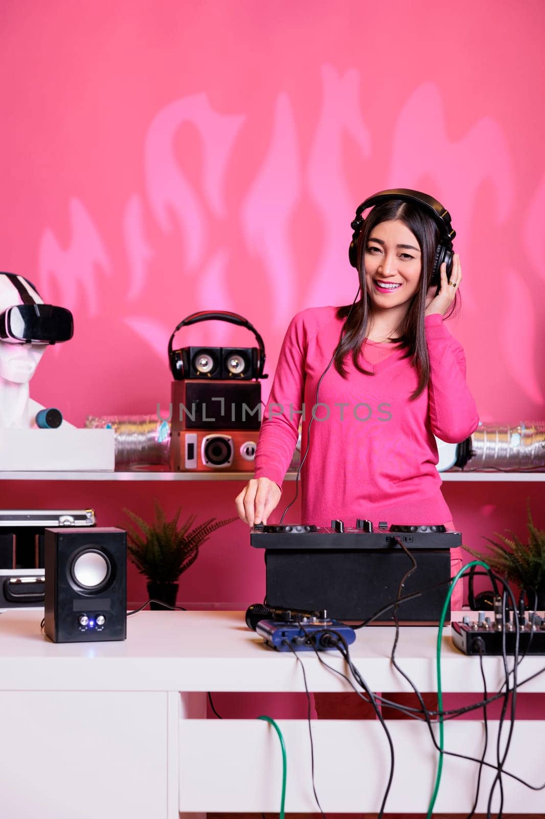 Artist wearing headset while mixing electronic sound with techno at professional mixer console, having fun at night in club. Asian musician standing at dj table performing music, celebrating album