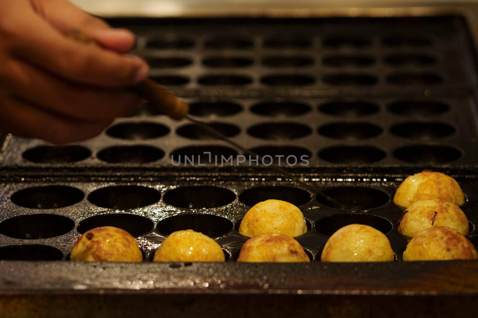 The cooking of Takoyaki. The popular Japanese street food that consists of small, ball-shaped snacks made of batter and filled with small pieces of octopus and other ingredients.