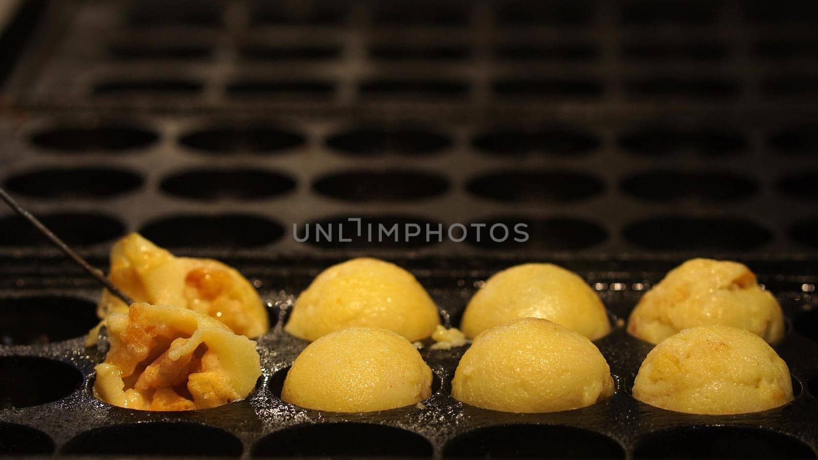 The cooking of Takoyaki. The popular Japanese street food that consists of small, ball-shaped snacks made of batter and filled with small pieces of octopus and other ingredients.