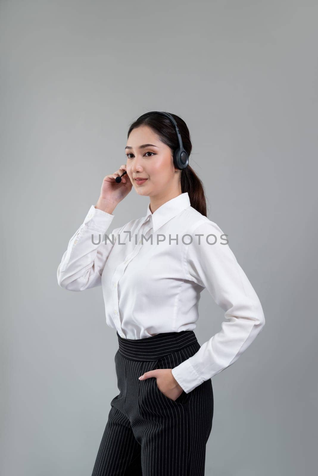 Attractive asian female call center operator with happy smile face advertises job opportunity on empty space, wearing a formal suit and headset on customizable isolated background. Enthusiastic