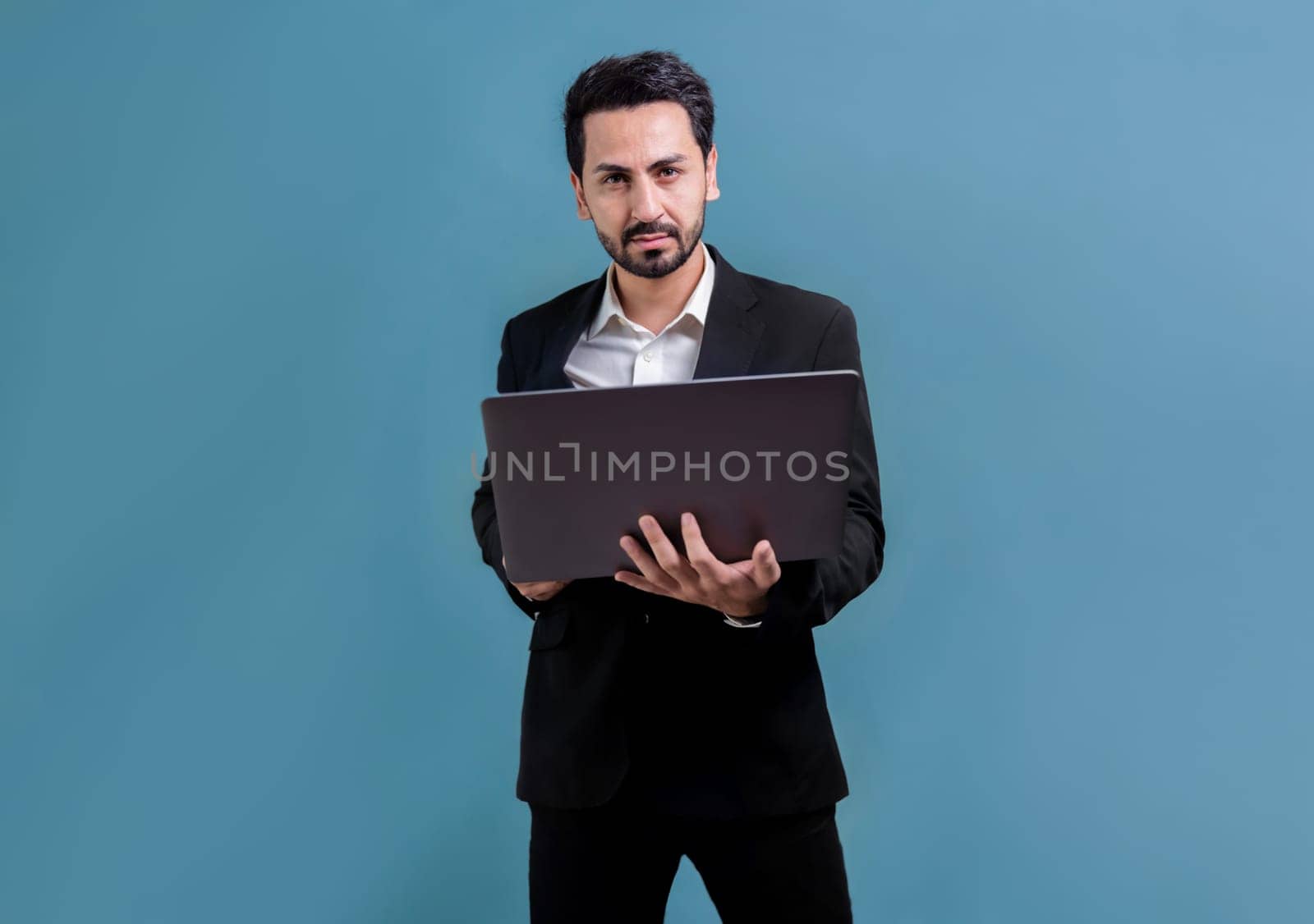 Successful businessman in black suit with innovative tech concept, standing pose and holding laptop and smiling with excitement on copyspace background for promotion or advertisement. Fervent