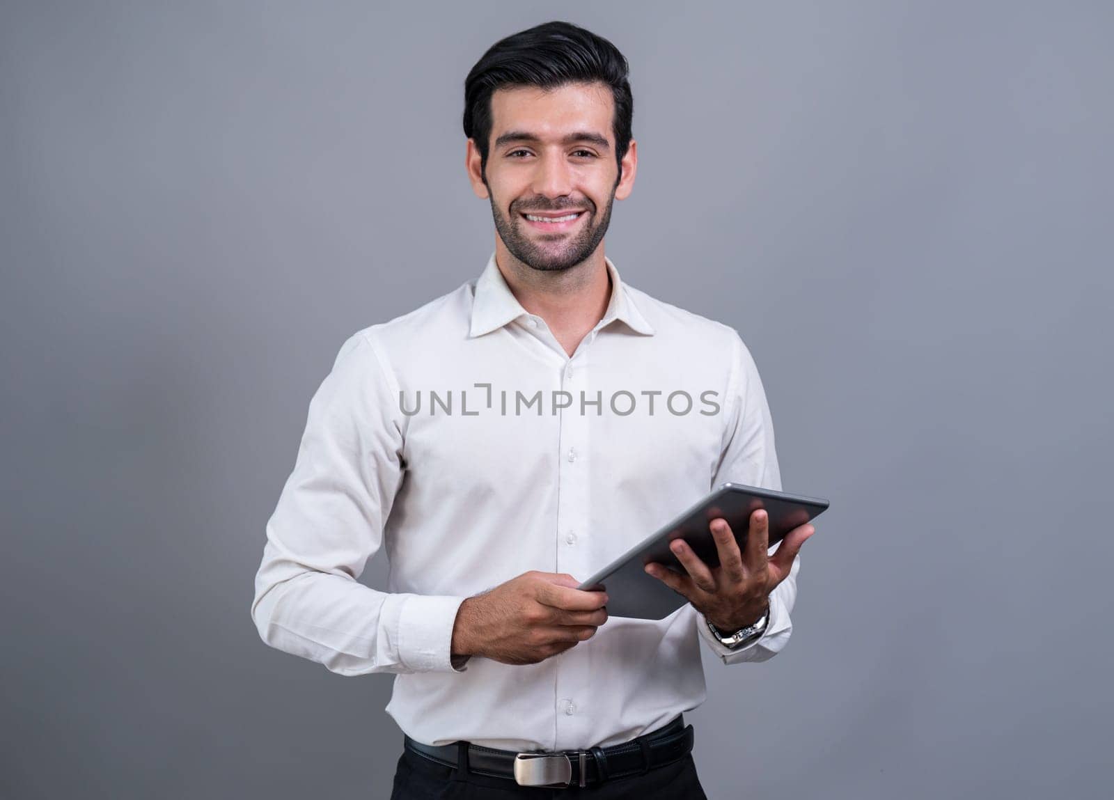 Confident businessman in formal suit holding tablet with surprise look for promotion or advertising. Facial expression and gestures indicate excitement and amazement on an isolated background. Fervent