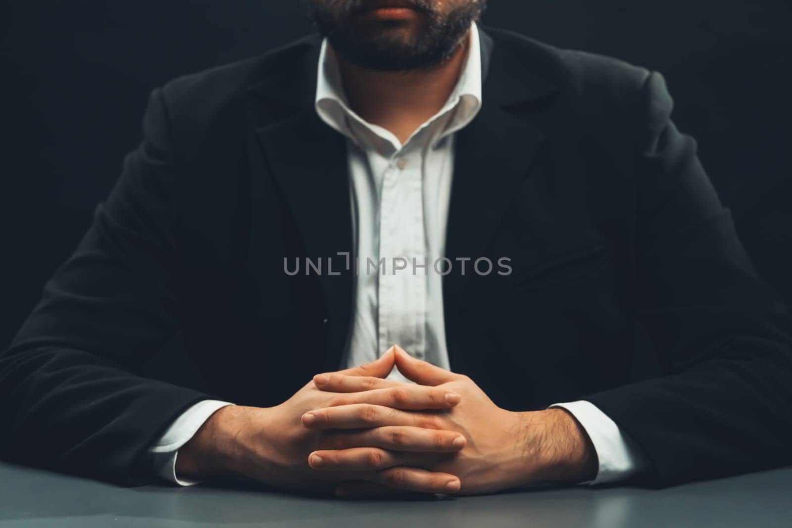 Businessman or lawyer wearing formal black suit sitting at table on isolated black background. Concept of a man with authority and seriousness gesture. equility