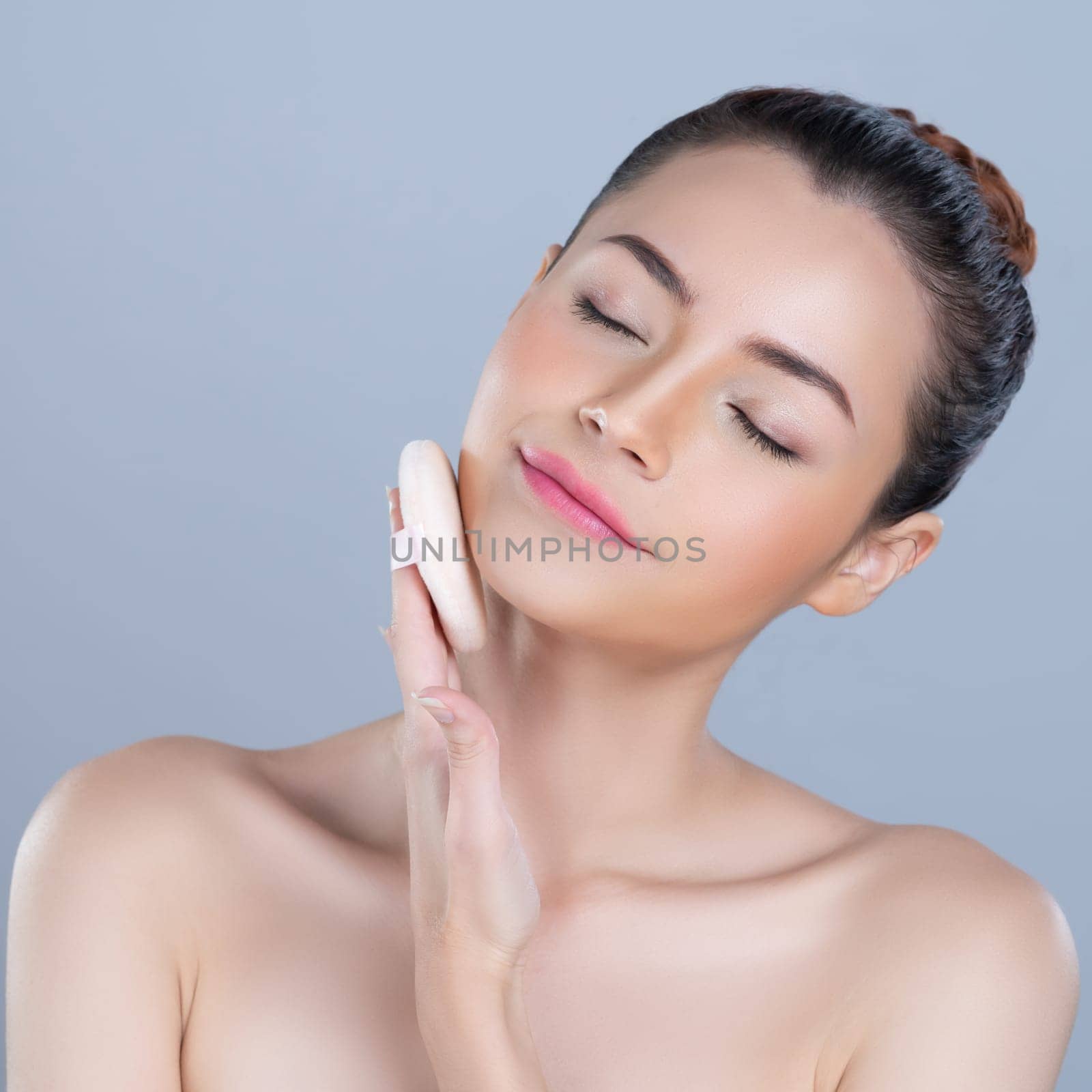 Glamorous beautiful female model applying cushion powder for facial makeup concept. Portrait of flawless perfect cosmetic skin woman put powder puff on her face in isolated background.