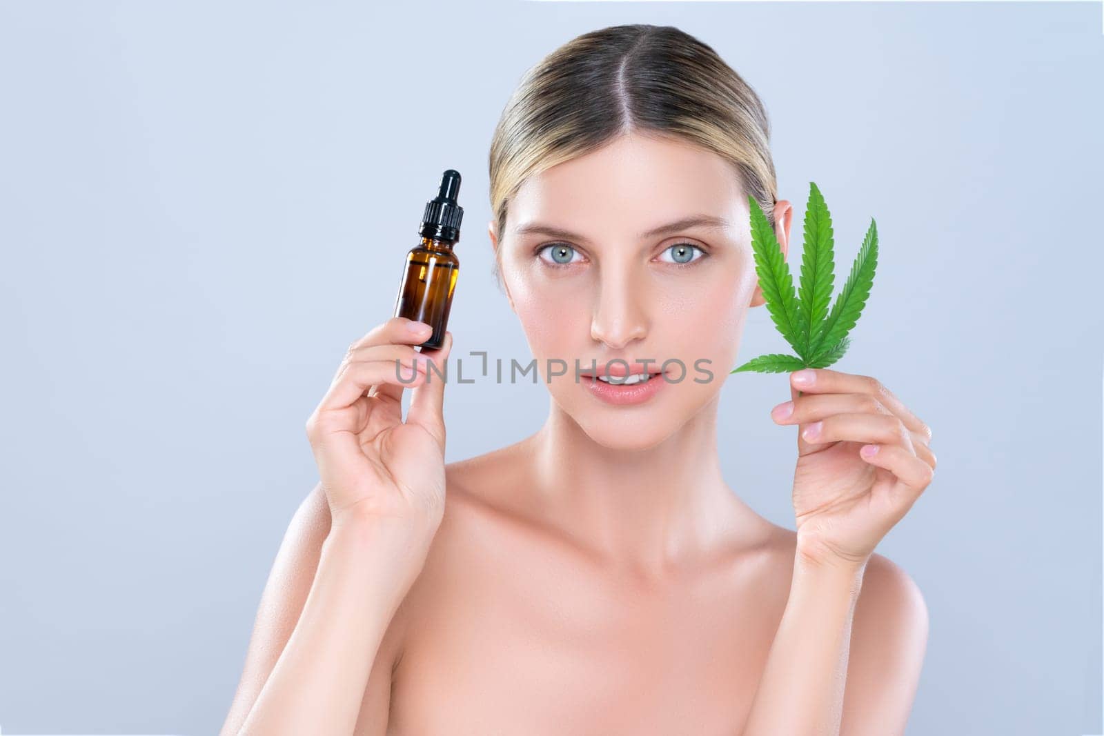 Alluring portrait of beautiful woman in isolated holding green leaf with marijuan extracted bottle for skincare treatment product. Cannabis CBD oil for cosmetology and beauty concept.