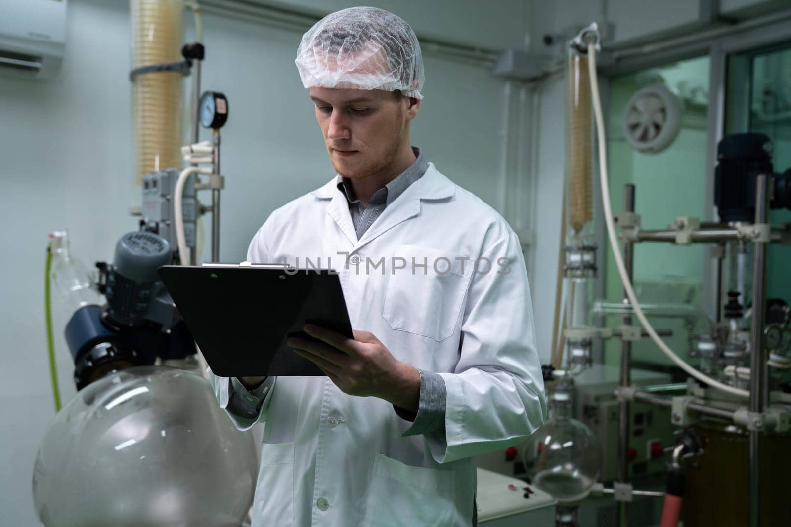 Apothecary scientist using a clipboard and pen to record information from a CBD oil extractor and a scientific machine used to create medicinal cannabis products.