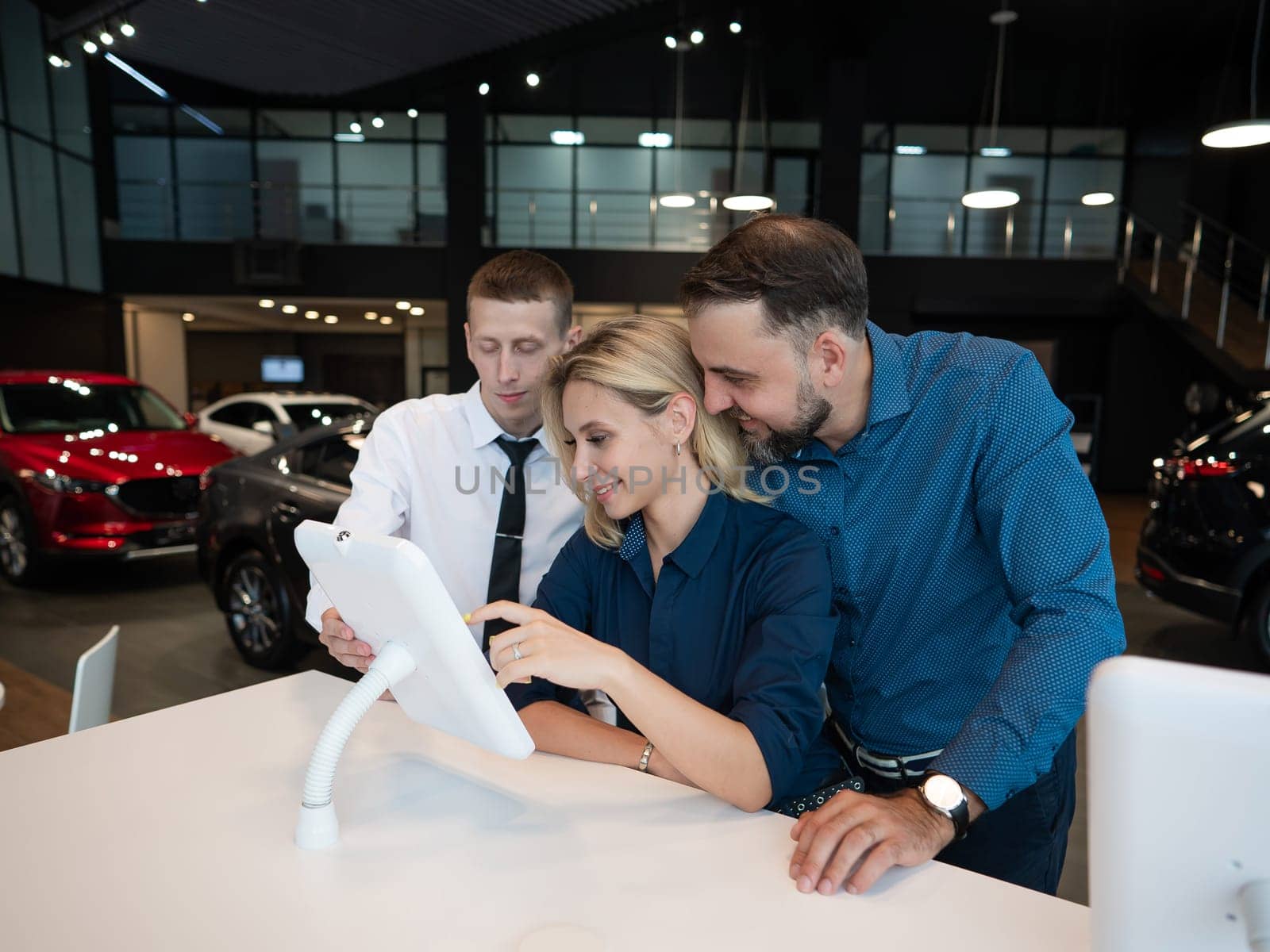 Caucasian married couple chooses a car in a car dealership on digital tablets. by mrwed54