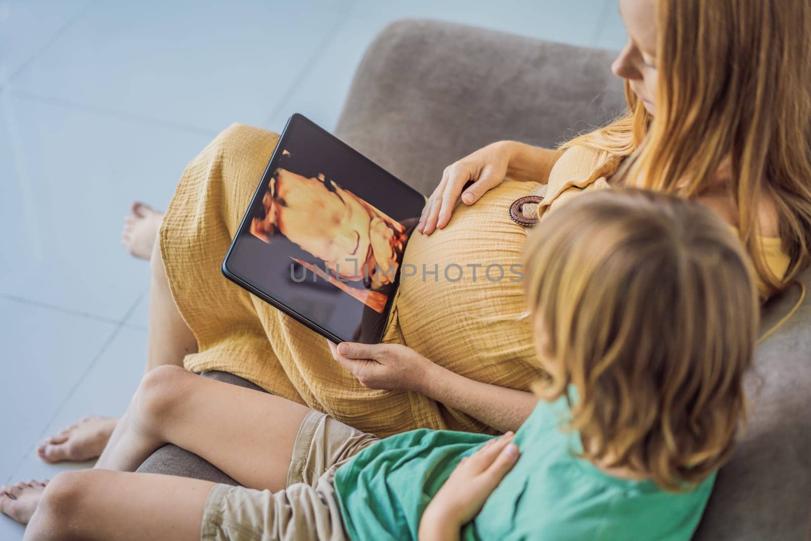 Mom and her son looking on ultrasound image of his unborn baby brother on mothers tablet. Concept of healthcare and family happiness expecting baby.