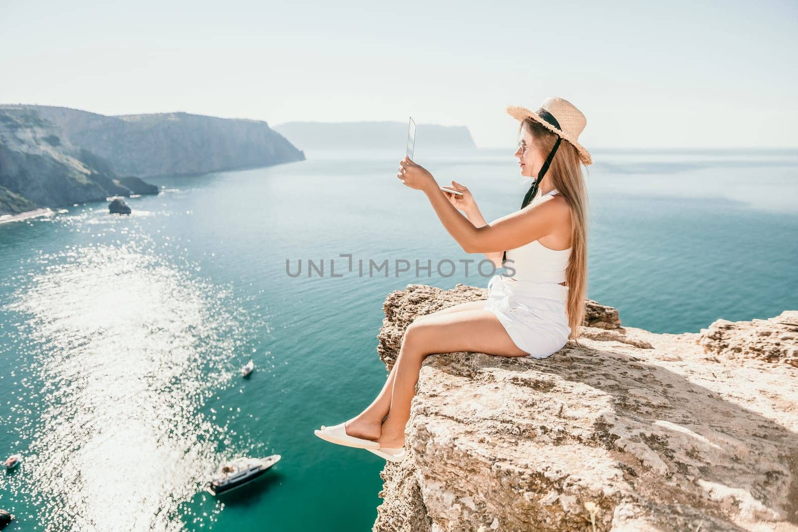 Woman laptop sea. Working remotely on seashore. Happy successful woman female freelancer in straw hat working on laptop by the sea at sunset. Freelance, remote work on vacation by panophotograph