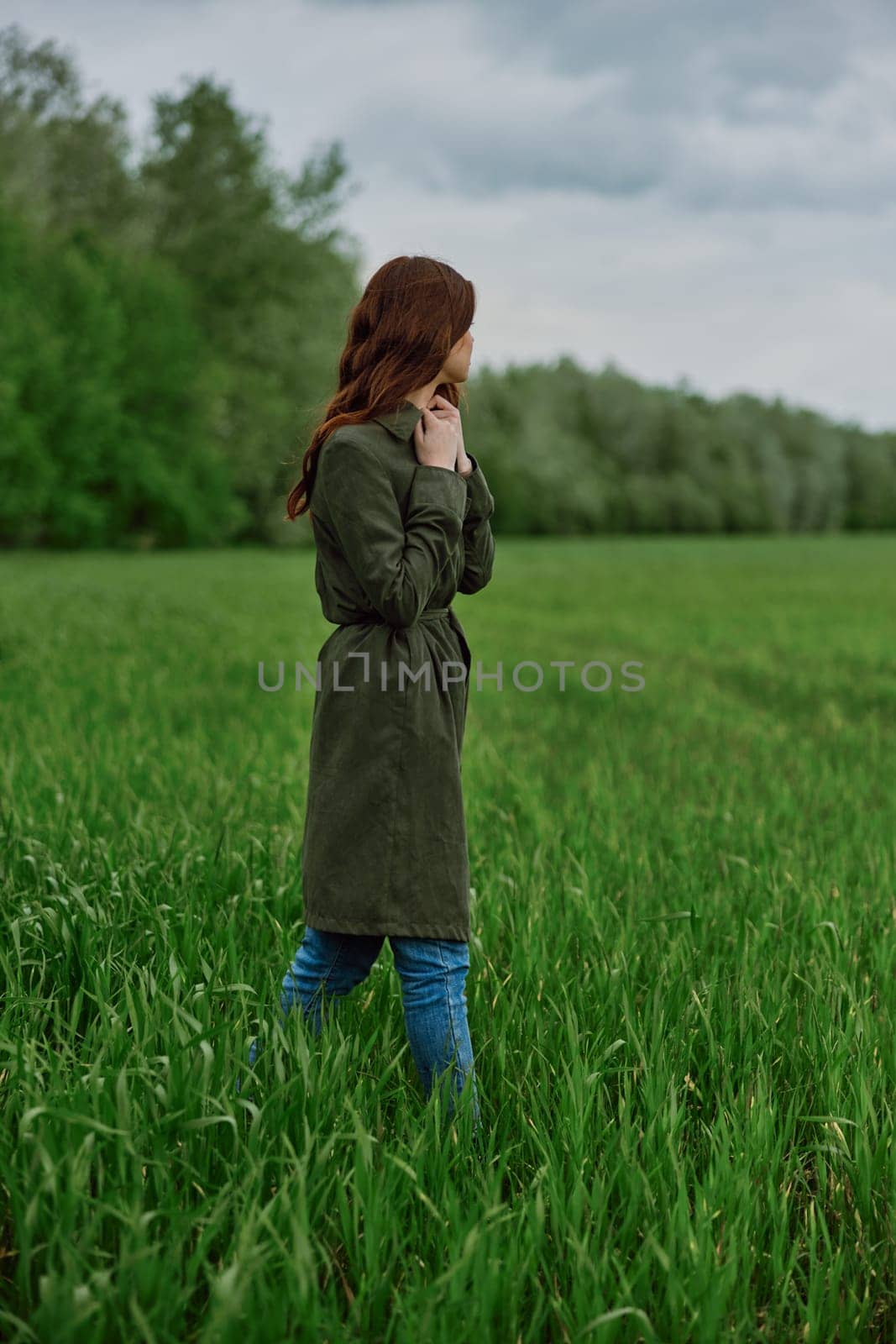 a woman in a long coat stands in a field in cold, windy weather in spring. High quality photo
