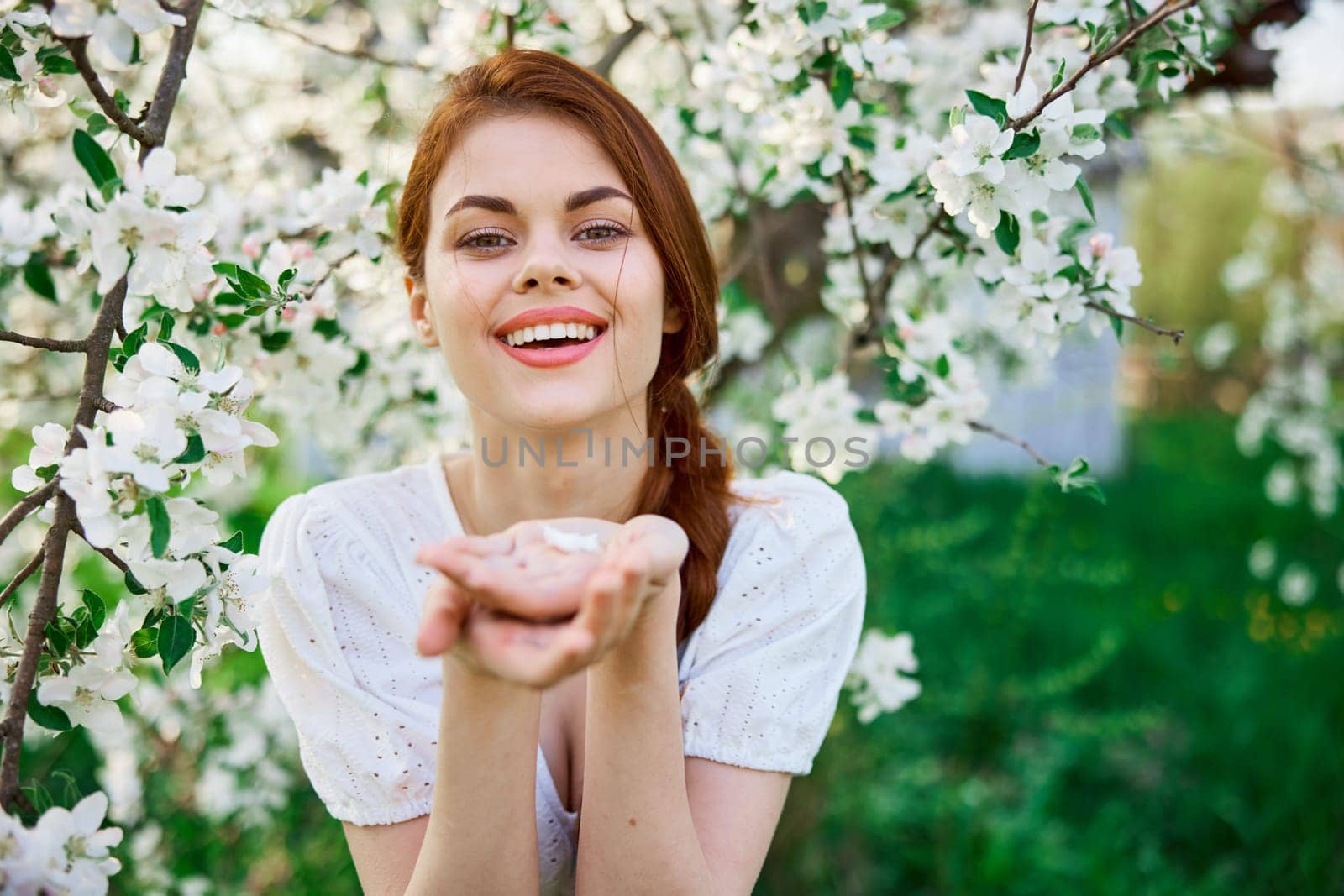 portrait of a beautiful red-haired woman against the background of a flowering tree with flowers in her palms by Vichizh