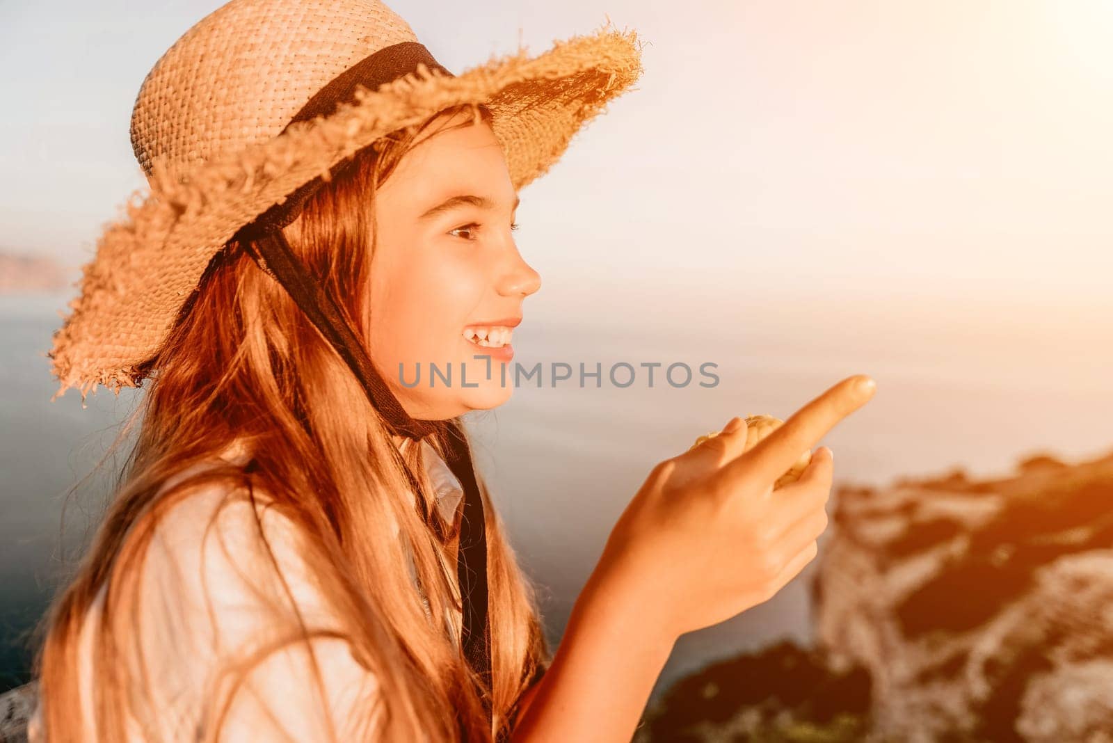 Happy girl eating corn. Summer snacking on the sea. Portrait of young beautiful girl in straw hat eating grilled corn while sitting by the sea on sunset time. Close up. Selective focus by panophotograph