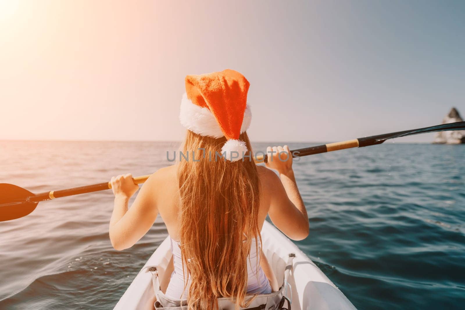 Woman in kayak back view. Happy young woman in Santa hat floating in kayak on calm sea. Summer holiday vacation and cheerful female people relaxing having fun on the boat. by panophotograph