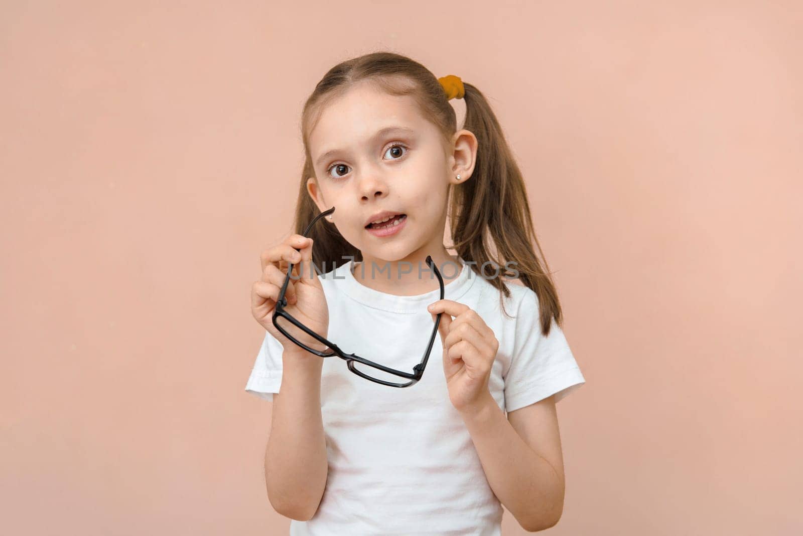 Cute caucasian elementary school age girl with poor eyesight holding diopter glasses in front of her.