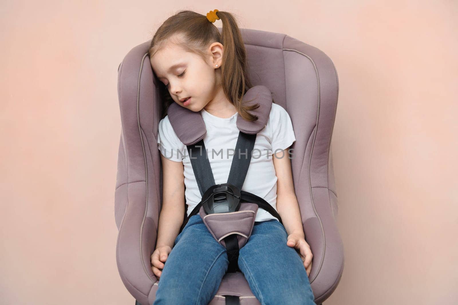 Preschool girl fastened sleeping in a car seat.